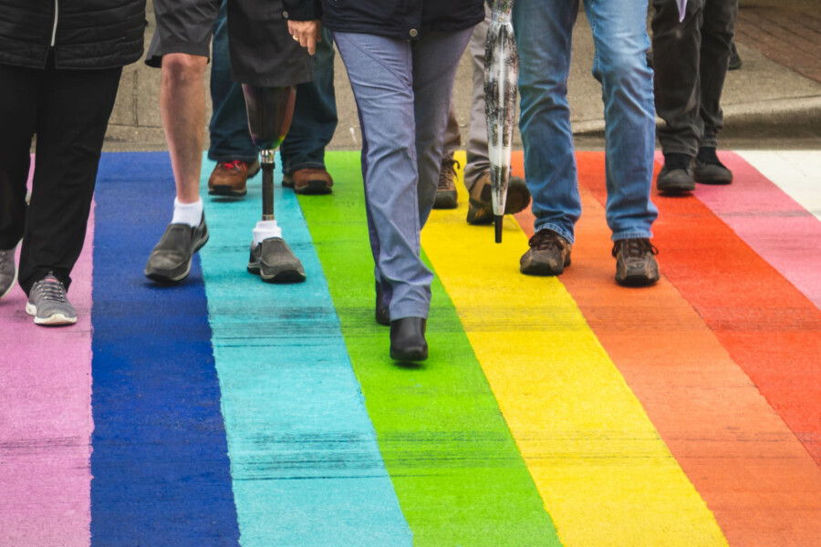 People crossing a rainbow crosswalk.